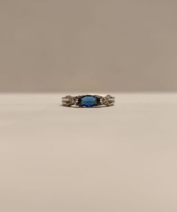 Anillo con circonia azul ovalada y circonitas cruzadas a los lados